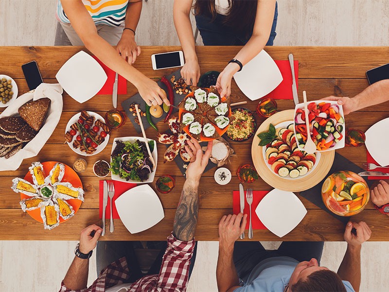 People eat healthy meals at festive table served for party. Friends celebrate with organic food on wooden table top view. Happy company having lunch, taking sandwiches from dish
