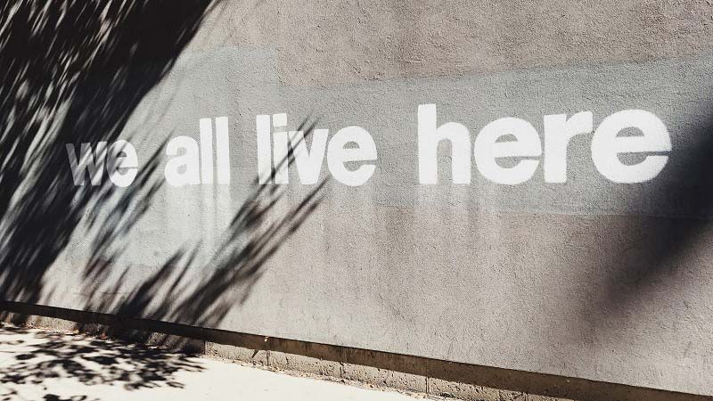 Text "we all live here" painted on the wall 