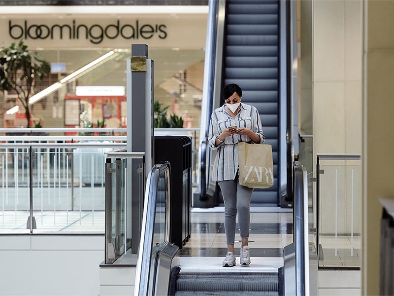 Woman coming down after shopping from escalator while using her phone in a shopping mall